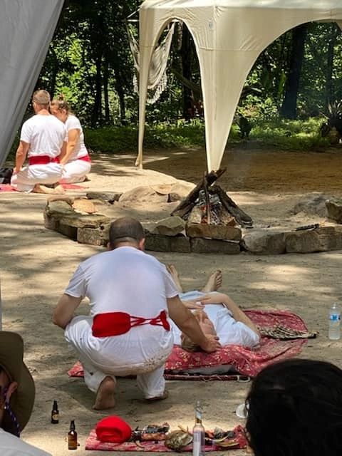 Facilitators in white with red sashes tending to participants lying on blankets at an outdoor ceremony